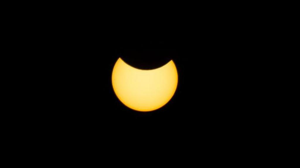 A picture of the sun undergoing a partial eclipse, with a dark crescent obscuring it from above.