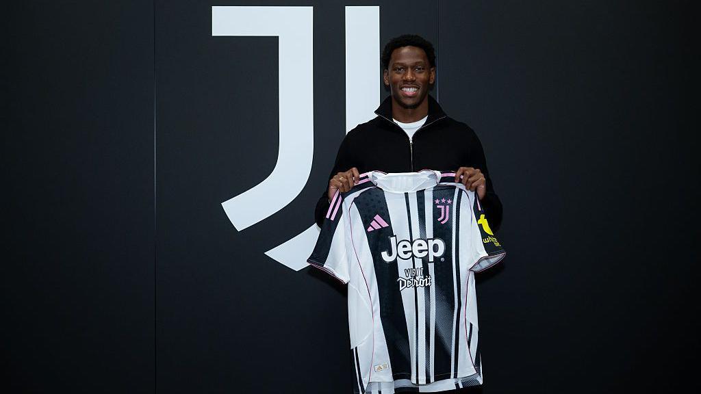 Jonathan David holds up a black and white Juventus shirt