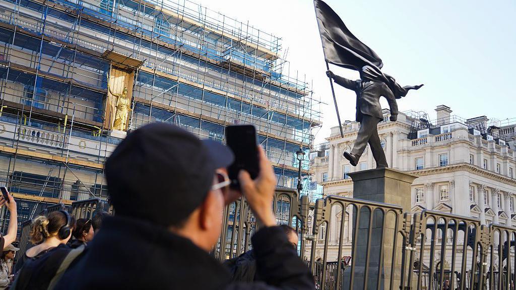 someone taking a picture of the statue surrounded by a safety barrier
