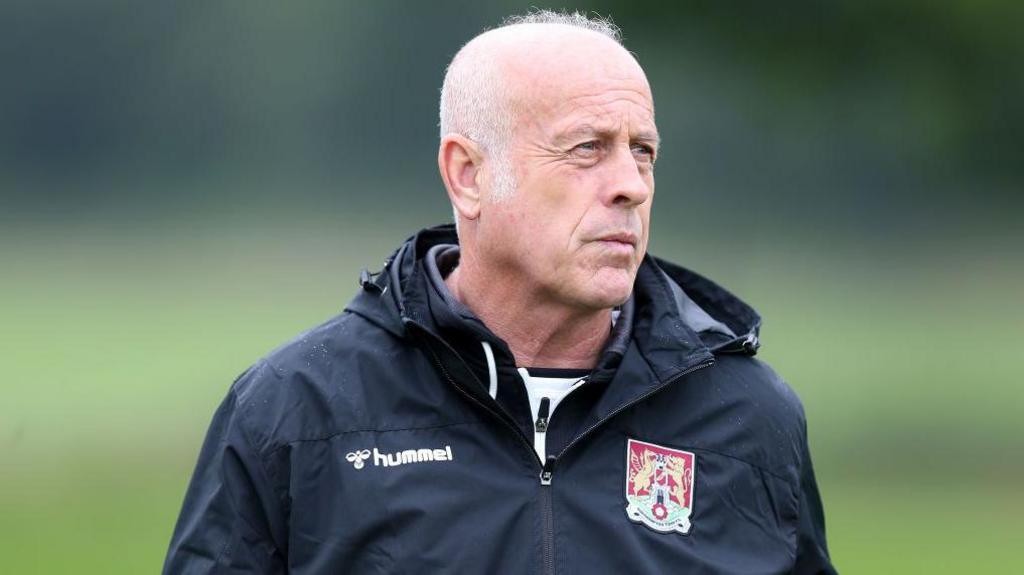Martin Foyle wearing a coat with a Northampton Town crest looking into the middle distance