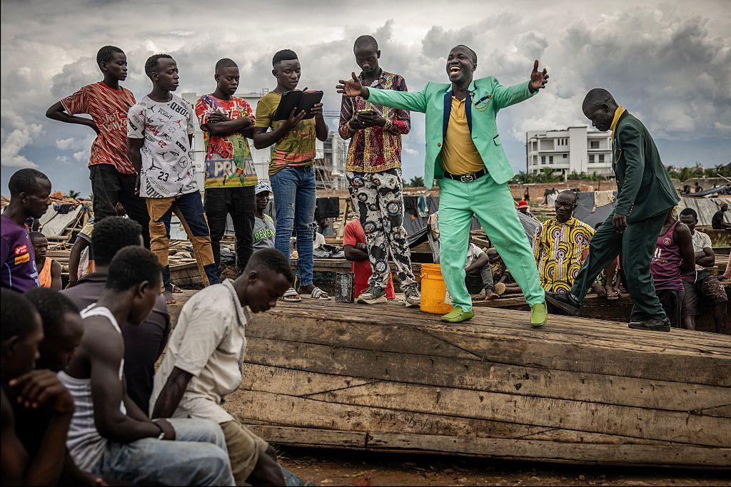 A man in a green suit on top of a boat, preaching to a crowd.