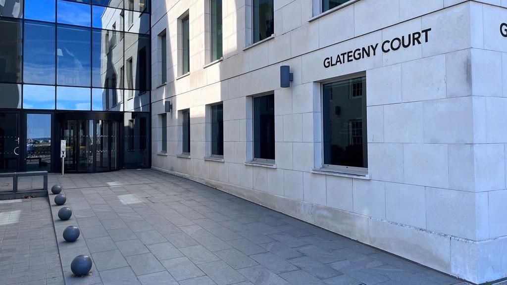 A modern finance building with an angular limestone facade on one wall and glass on another. A sign reads Glategny Court. Small stone spheres line one side of the courtyard.