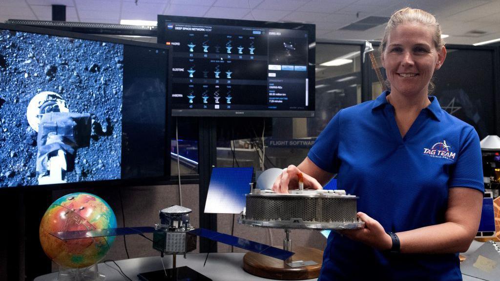 woman holding asteroid sample, next to computer showing results and detailed charts