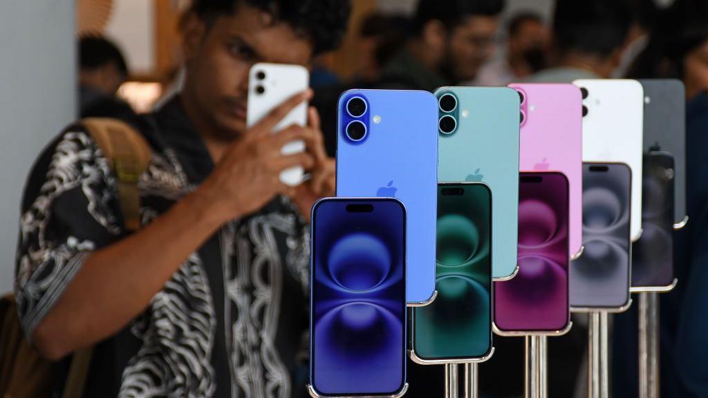 A man seen using his phone next to iPhone 16 models kept on display at the Apple store in Bandra Kurla Complex (BKC) in Mumbai.
