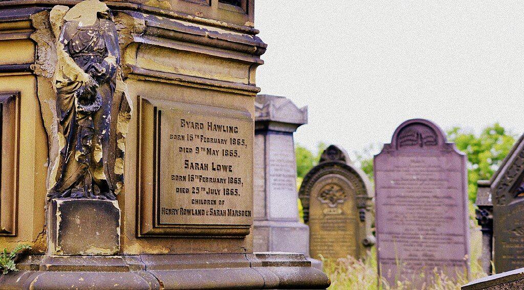 A cemetery with headstones. In the foreground is a large monument with damaged angels on it.