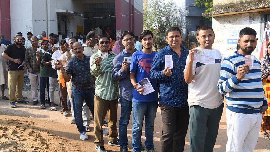 Men show their voter ID cards as they stand in a queue outside a polling station in Bihar's Danapur.