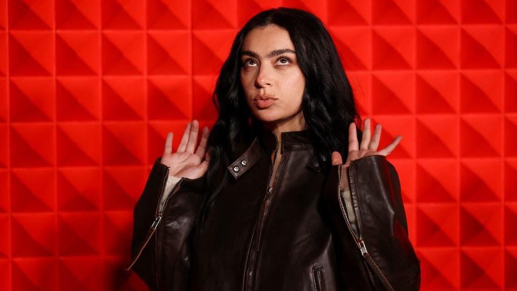 Woman wearing a black leather jacket stands against a red background