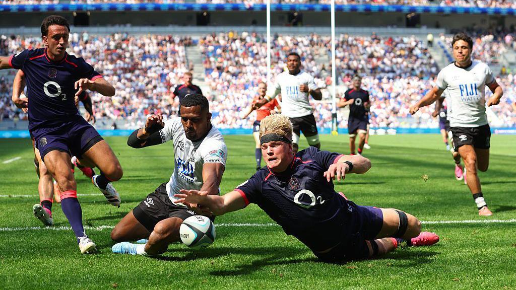 Henry Pollock is about to score his first try, beating Jiuta Wainiqolo to the ball to touch down as players from each side watch the pivotal moment