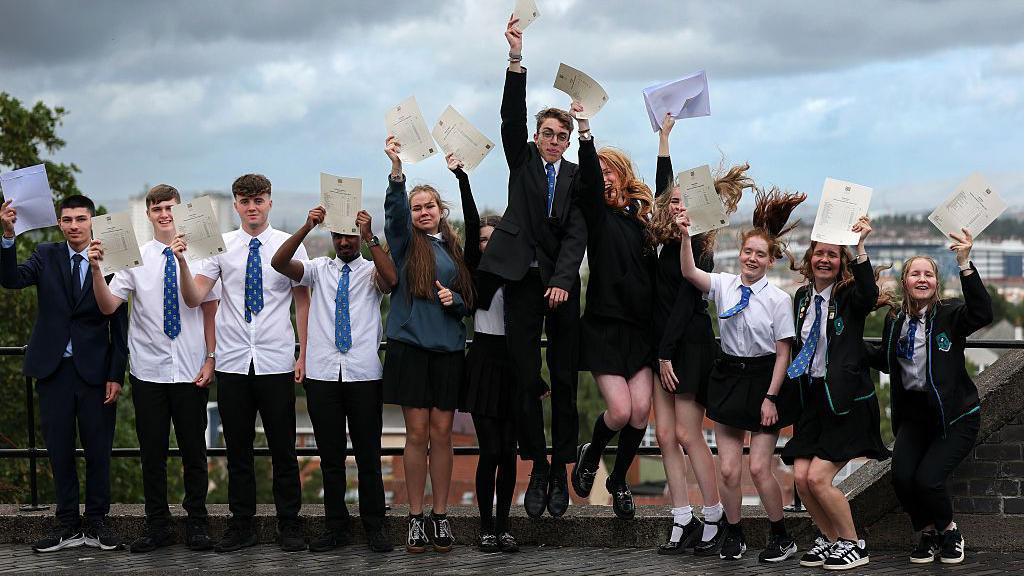 Students smiling and jumping holding their a-level results 