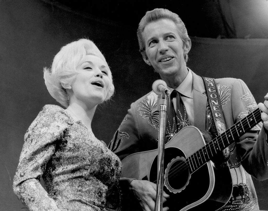 Black and White image of Dolly and Porter singing into a shared microphone, and he is playing a guitar.