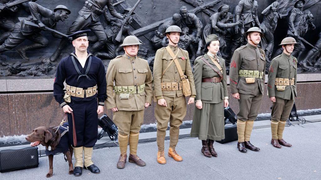 Six soldiers dressed in World War One uniforms standing in front of the sculpture