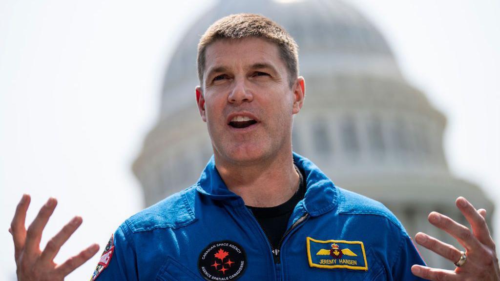 Jeremy Hansen wearing a blue jacket talking with his hands in front of him