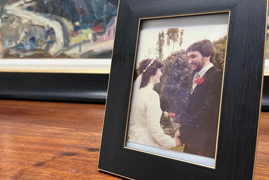 A wedding photo on the shelf in a black frame. It shows the couple smiling and holding hands, Afryl in a white dress, Aled in a black suit. 