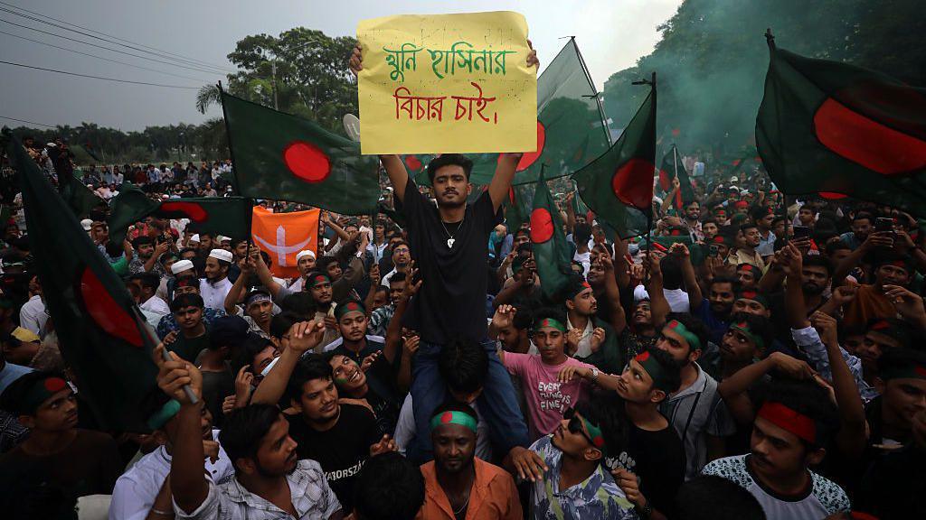 Bangladeshis wave the national flag 5 August, 2025 as they celebrate one year since Sheikh Hasina was ousted from power