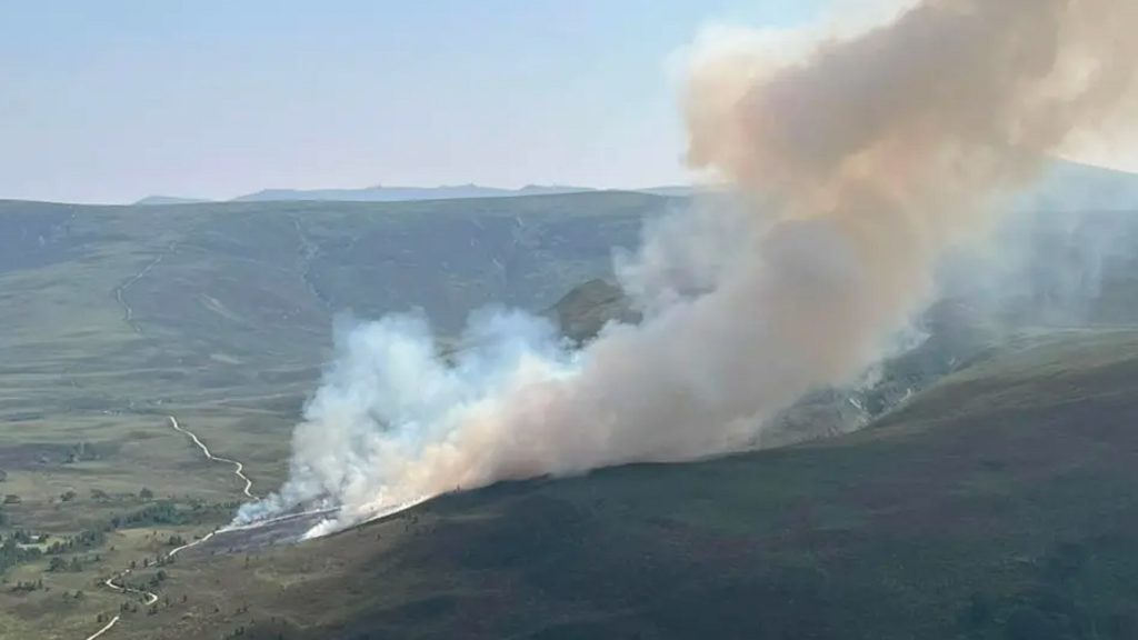 smoke billowing from a large wildfire across a hill range