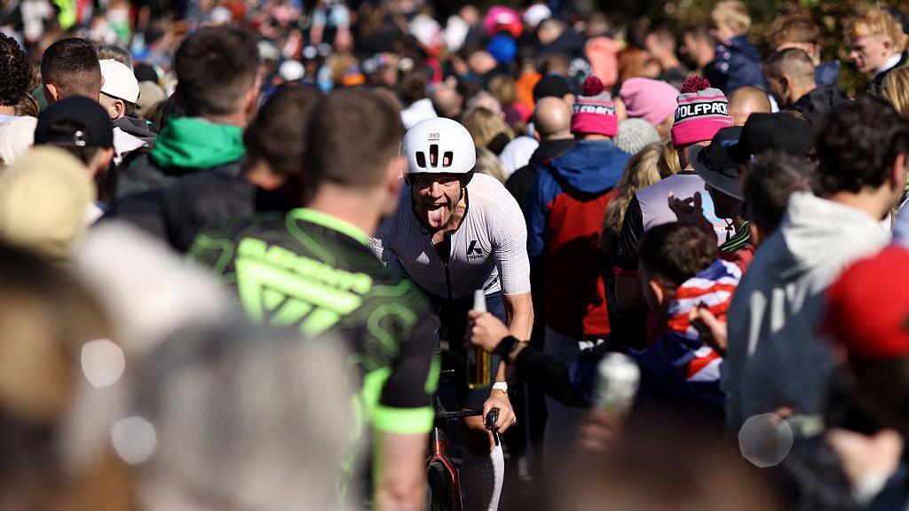 A cyclist sticks ut his tongue as he passes between crowds of people
