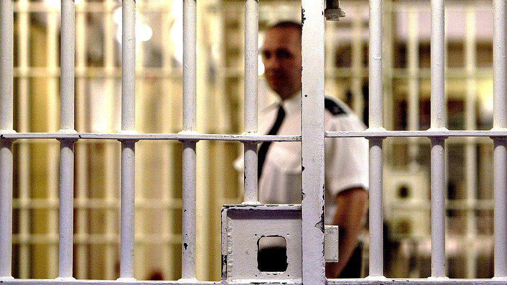 A prison guard at HMP Pentonville stands behind a locked gate 