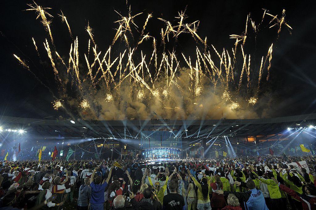 Fireworks light up the sky during the closing ceremony of the 2014 Commonwealth Games at Hampden Park. A large crowd is gathered outside the stadium and many people are raising their hands in celebration.