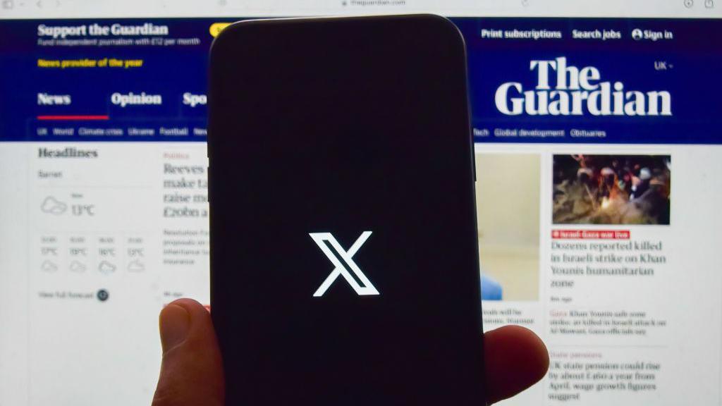 A person holds a phone with the X logo in front of the Guardian's homepage.