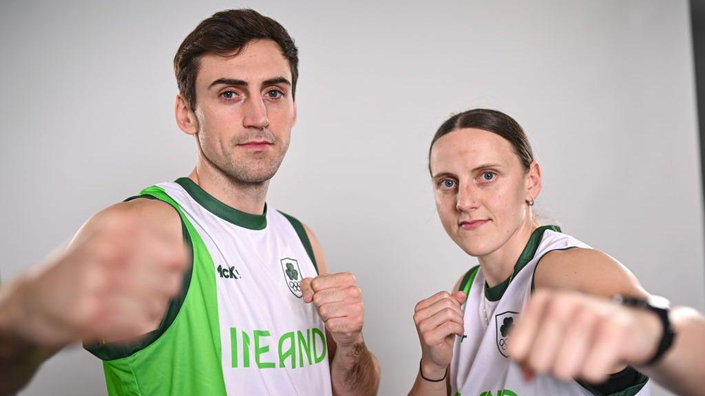 A man and a woman are pictured holding their fists in a boxing pose for a promotional image. They are both dressed in sleeveless green and white Team Ireland tops with the word 'IRELAND' on the chest.