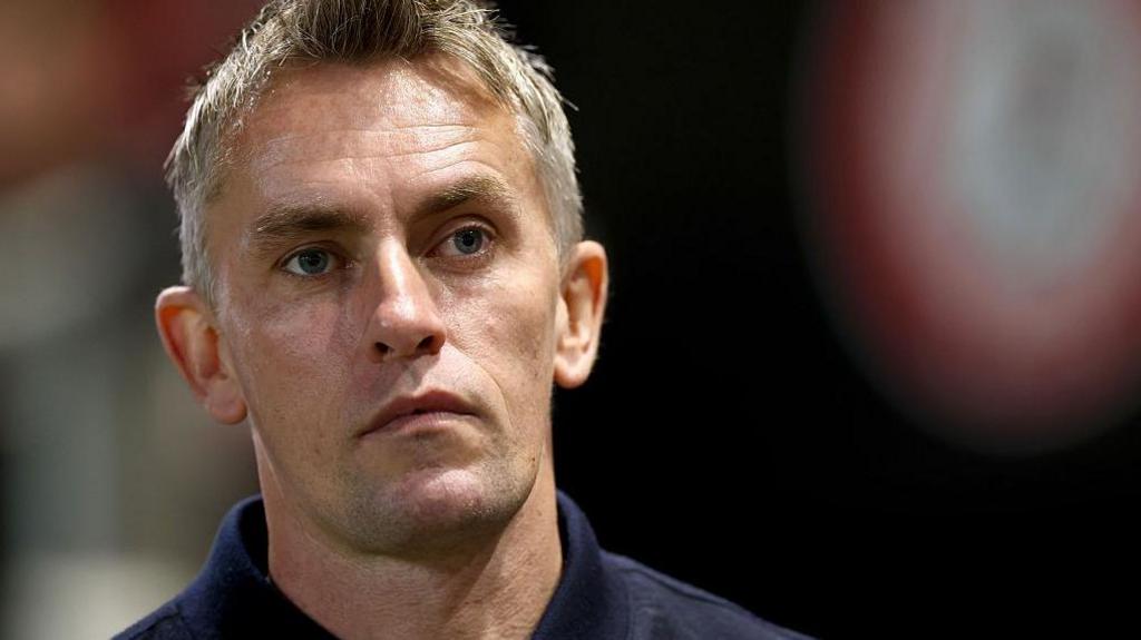 A close up of Ipswich Town manager Kieran McKenna. He's wearing a blue top and looks deep in thought