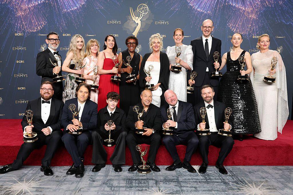 The cast and crew of Adolescence pose with their Emmy trophies on a red carpet stage while wearing formal clothing.