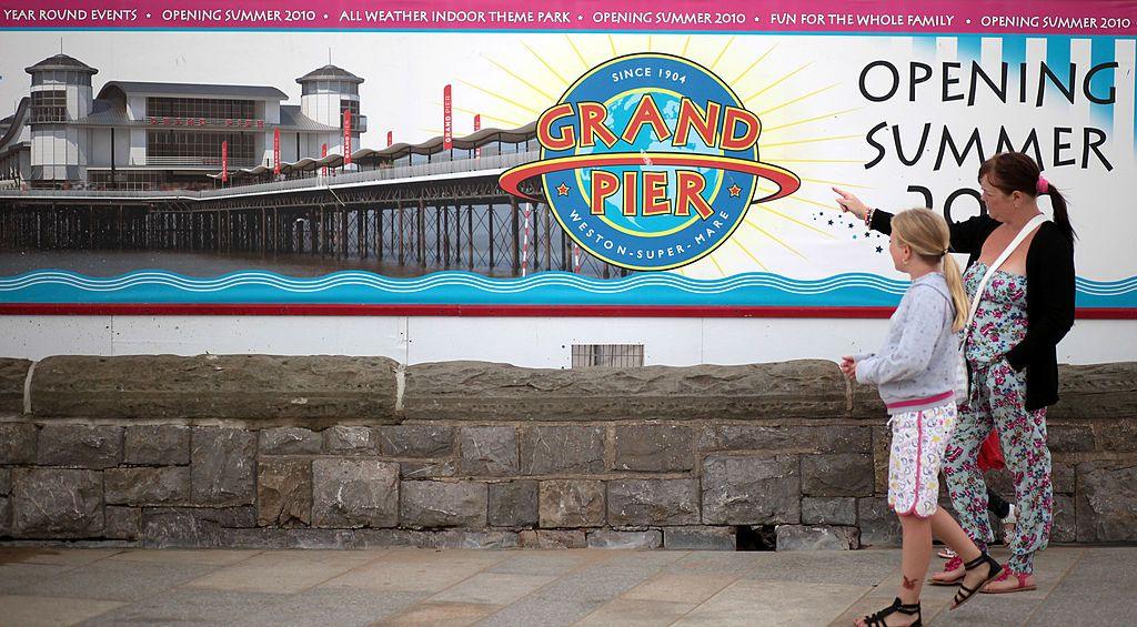 People pass hoardings erected in front of the entrance to the rebuilt Weston Grand Pier on August 20, 2010