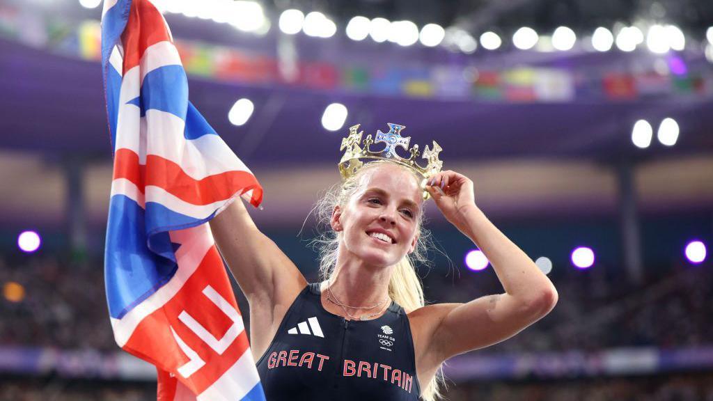 Keely Hodgkinson holding a GB flag and wearing a gold crown after winning the Women's 800m Final at last year's Olympic Games in Paris.