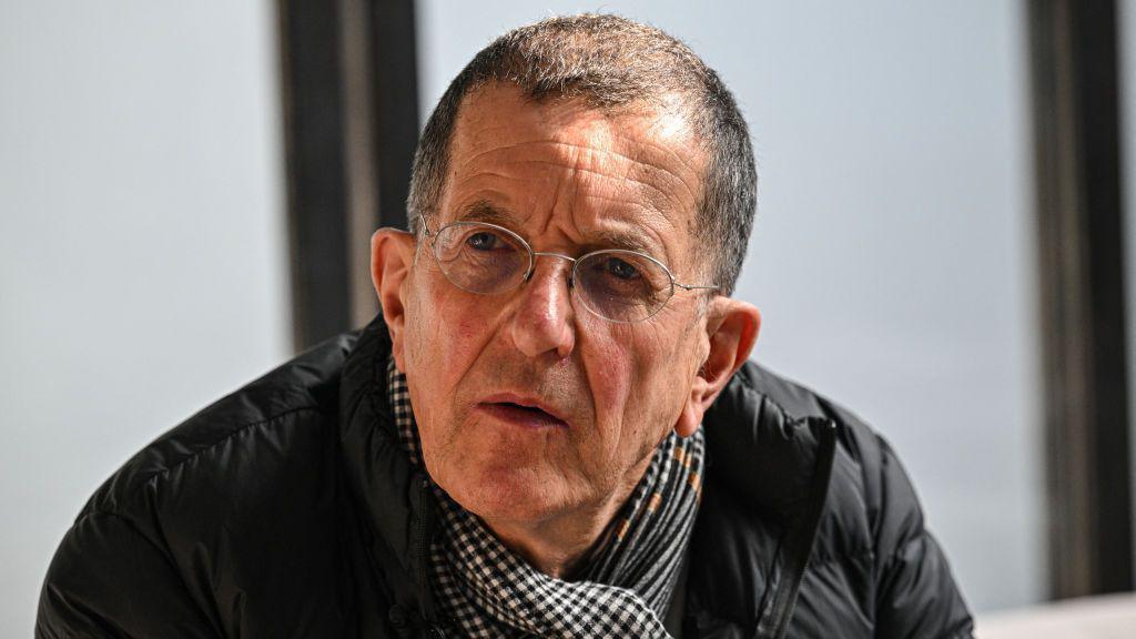 A close-up image of Sir Antony Gormley. He has short dark hair and is wearing wire-rimmed glasses, a black jacket and a checked scarf.