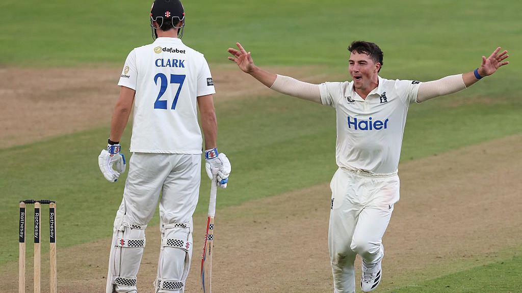 Warwickshire fast bowler Michael Booth celebrates taking the wicket of Sussex's Tom Clark at Edgbaston. He is running towards his team-mates who are out of the picture with his arms out stretched. The batter has his back to the viewer with his name and the number 27 on his shirt.