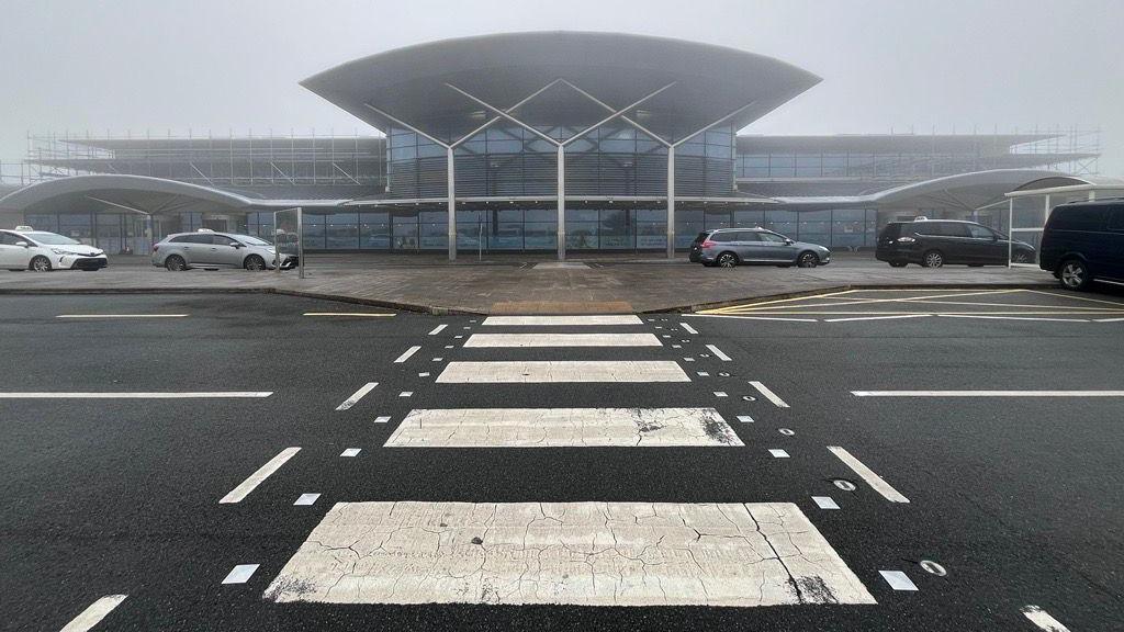 A zebra crossing leading up to an airport terminal, with heavy fog.