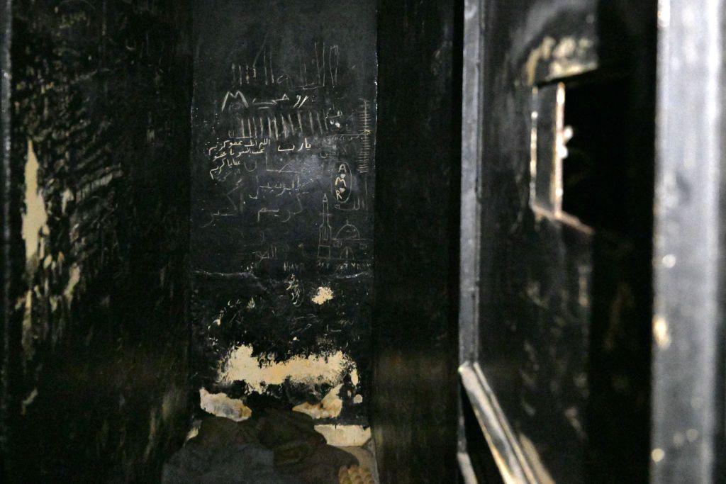 Writing on the walls of a black prison cell in the basement of Al-Khatib. There are blankets on the floor