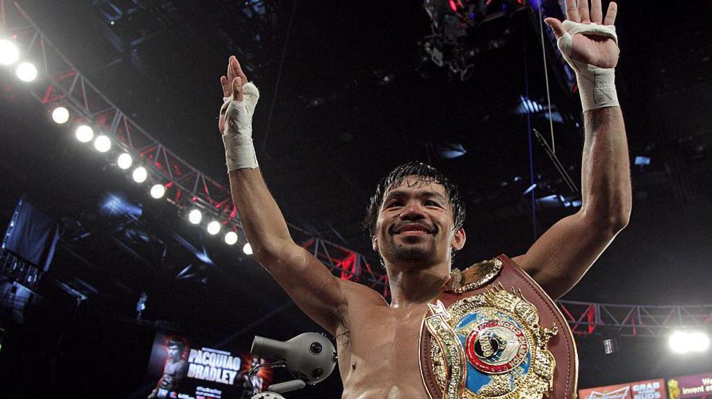 Manny Pacquiao raises his arms after winning a fight in the boxing ring with a championship belt on his shoulder