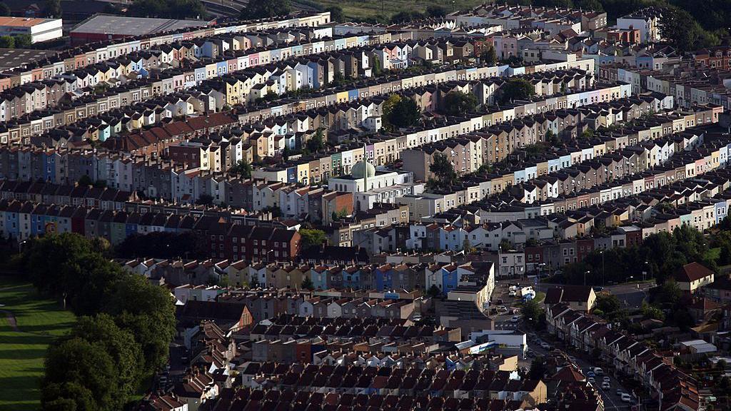 An aerial view of tightly packed colourful terraced houses in Bristol seen from the sky. The green grass and trees of Victoria Park is visible on the left-hand side of the picture