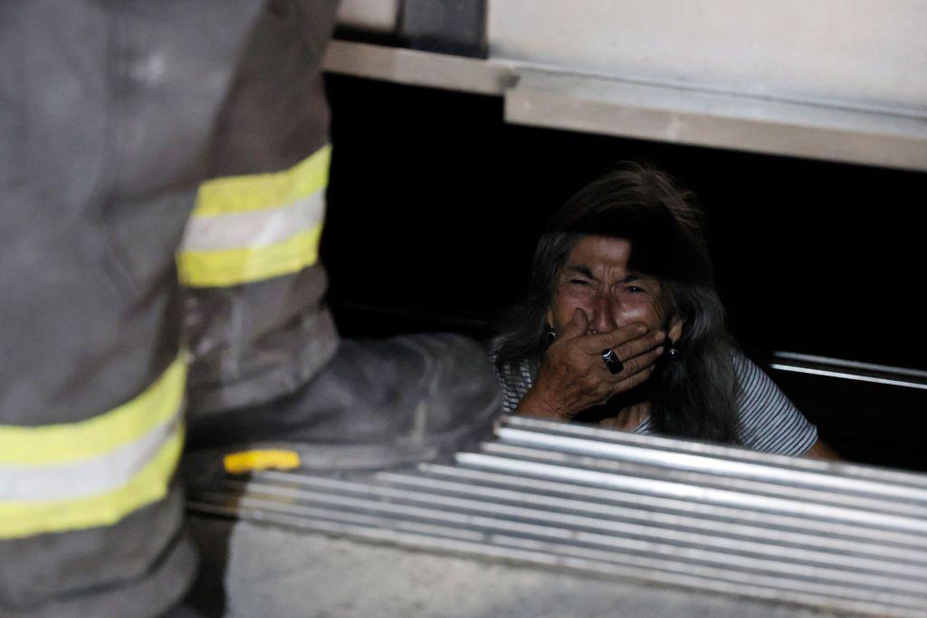 A woman is freed from the lift she was trapped in during the power cut in Chile. She is crying and holding a hand over her mouth as firefighters free her. 