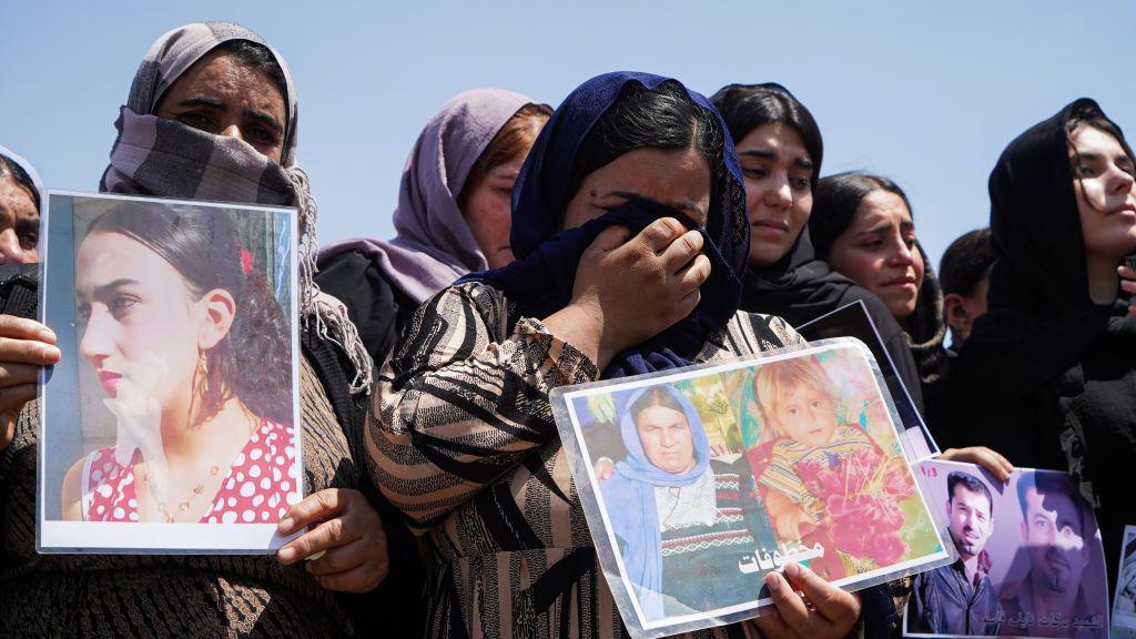 Iraqi Yazidi women cry as they hold pictures of missing relatives during a ceremony in Chamishko camp, in the Kurdistan Region of Iraq, on the 10th anniversary of the IS Yazidi genocide (1 August 2014)