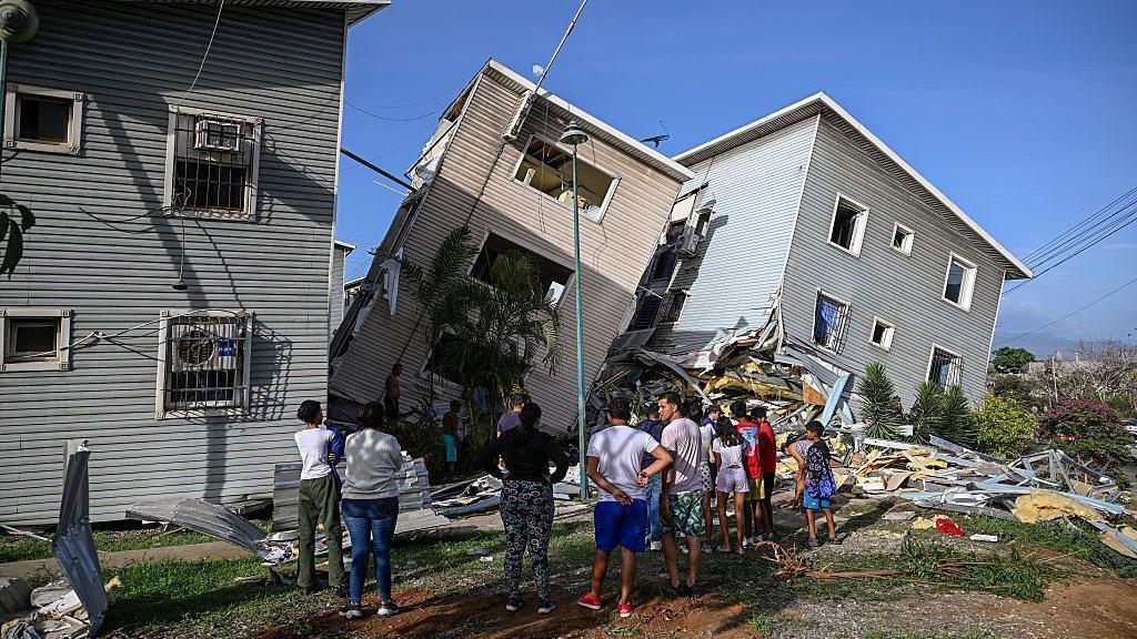 People look on at houses that have tipped heavily to the side and are now leaning, in Catia La Mar, La Guaira state 