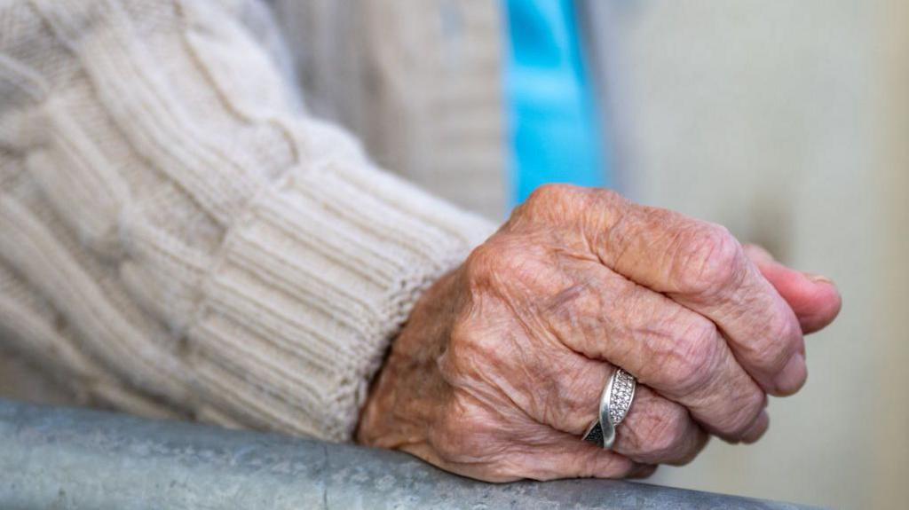 An elderly person's hand on a bannister