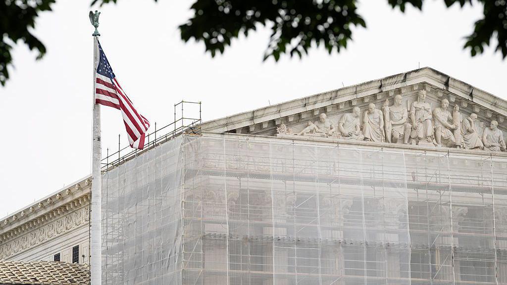 The exterior of the US Supreme Court with an American flag in foreground