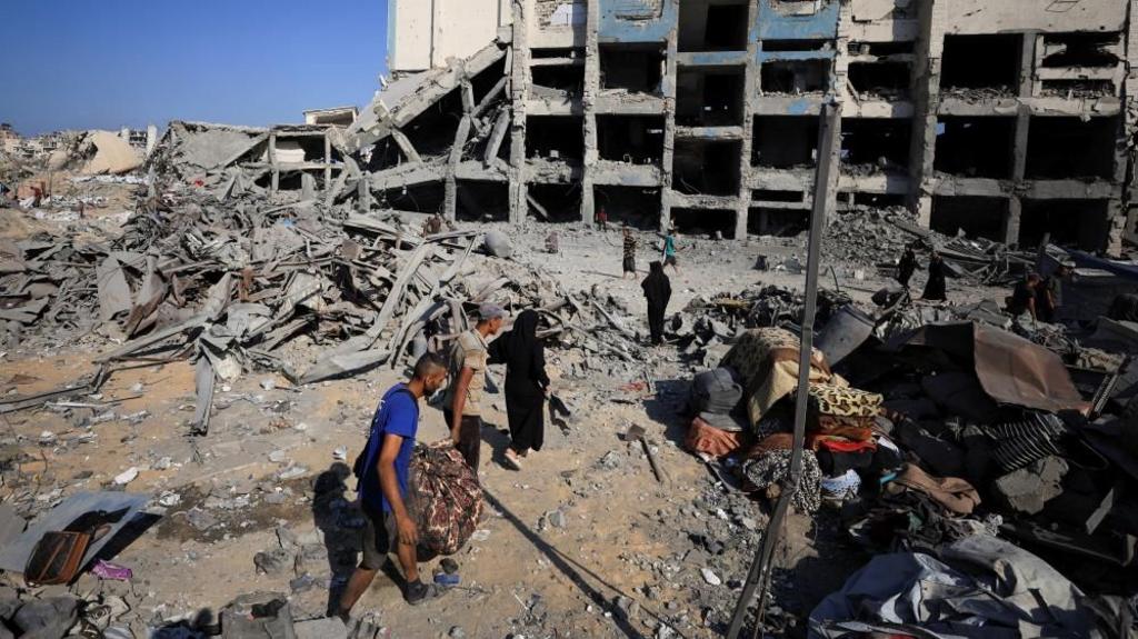 palestinians look through the rubble of a building in Gaza. tents of displaced people can be seen in the foreground.