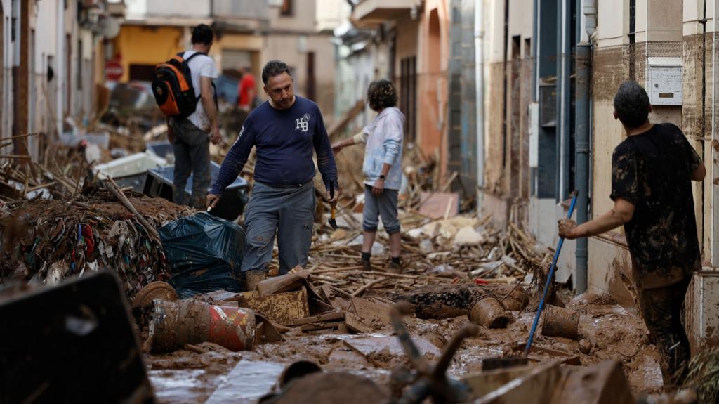 Residents wade through mud and clean their homes on a street filled with debris