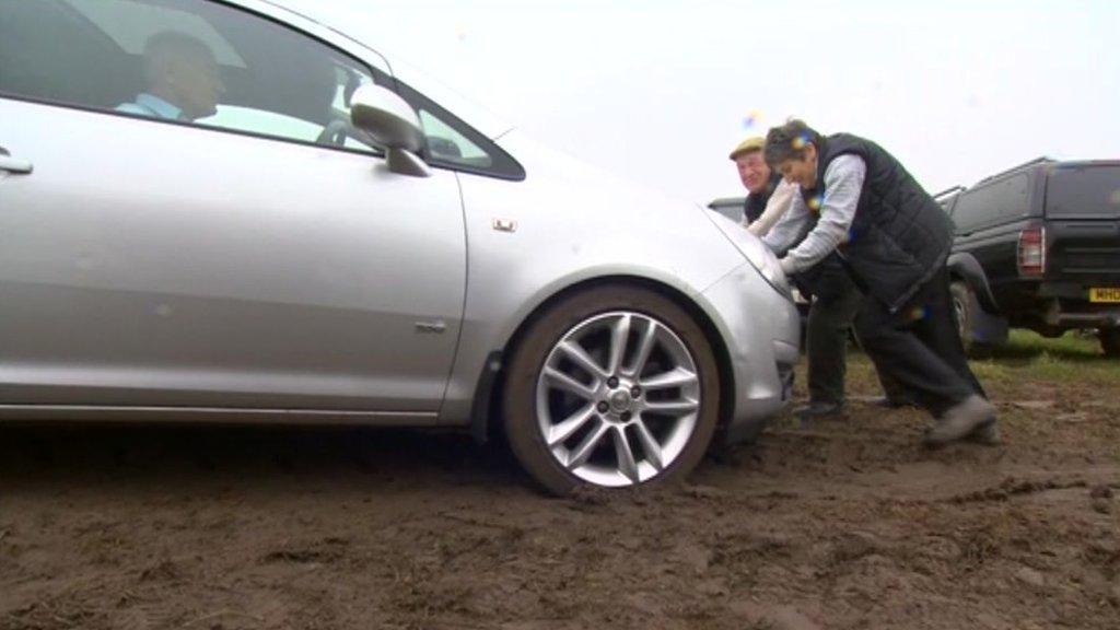 Two people pushing a car in a muddy field