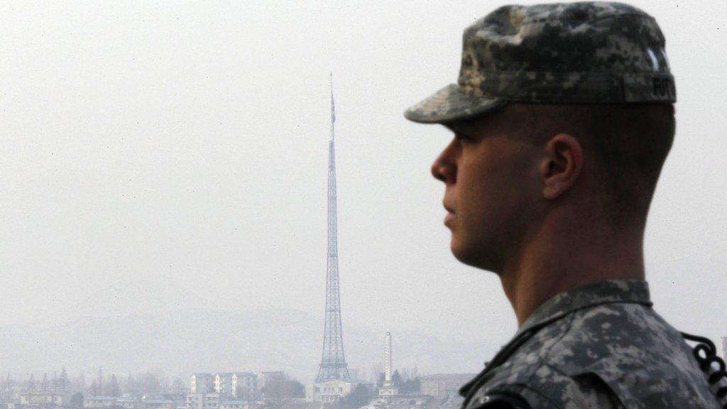 A US soldier is seen in the foreground of a huge North Korean flag hung at half-mast in the North Korea's propaganda village of Gijungdong, 28 December 2011