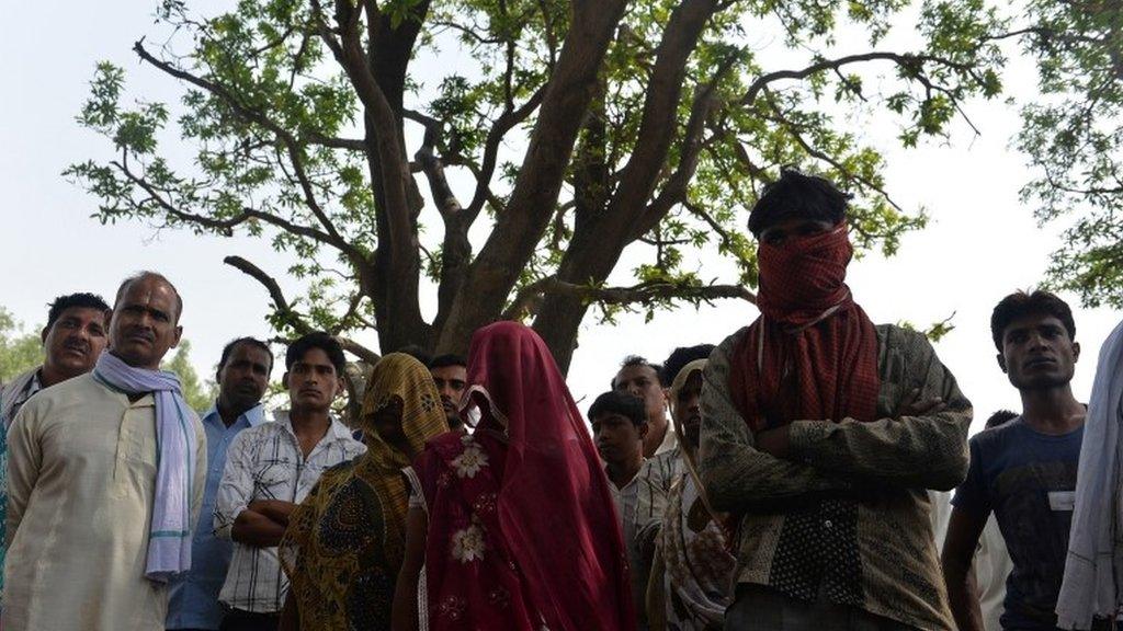 In this May 31, 2014, photo mothers of gang-rape victims (C, shawls covering their faces) and villagers stand in front of the mango tree where the girls were hanged in Katra Shahadatgunj in Badaun district