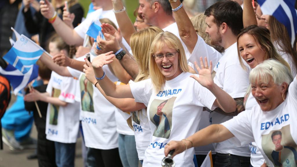 Supporters of Batonbearer 056 Edward Fitzpatrick wave as he carries the Glasgow 2014 Queen's Baton through Dennistoun in Glasgow.