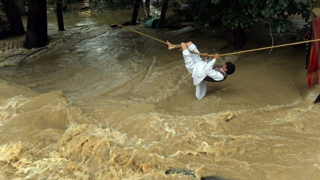 An Indian Kashmiri man crosses over flood waters with the use of a rope in Srinagar on September 9, 2014.