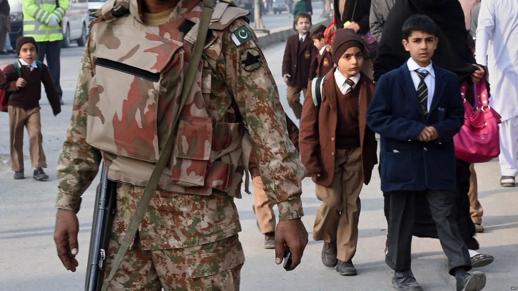 A Pakistani soldier stands guard as parents leave with their children near the site of an attack by Taliban gunmen on a school in Peshawar on 16 December 2014