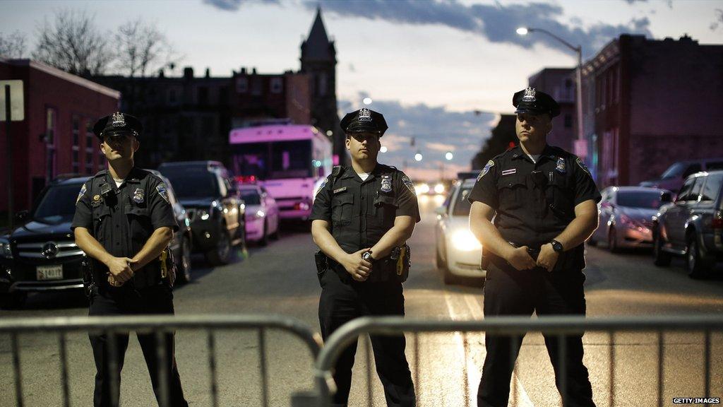 Three police officers stand on a street in front a barricade