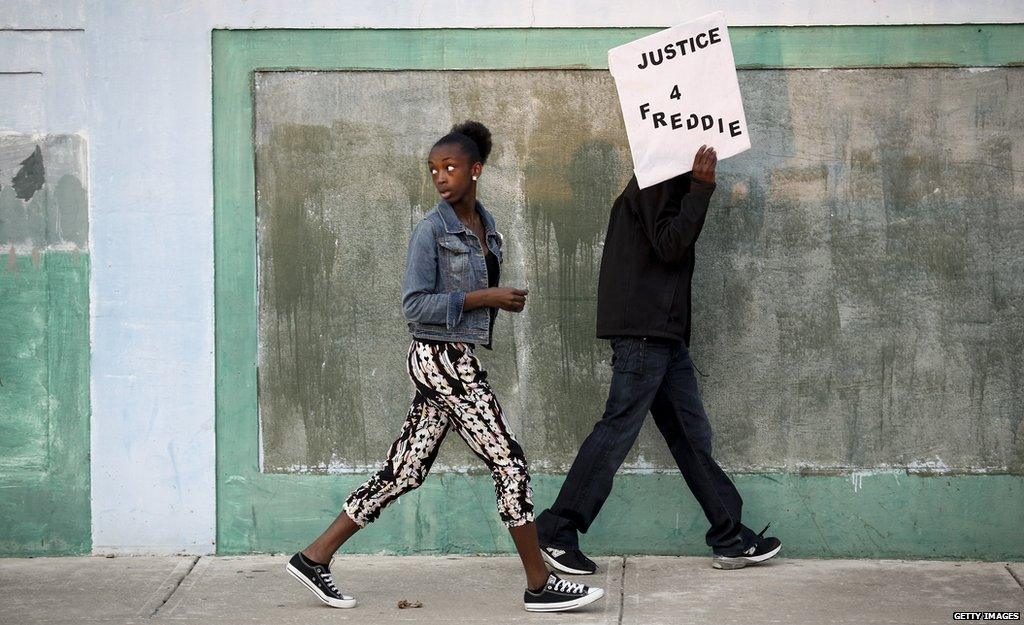 Two people walking. One holds a sign that says "Justice 4 Freddie"