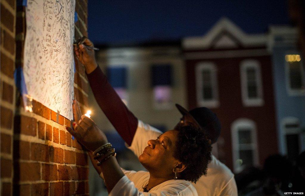 A woman uses a candle to read a sign while a man writes on it